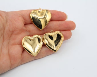 May include: Three gold heart-shaped locket pendants. The lockets are open and the inside is visible. The lockets are on a hand.