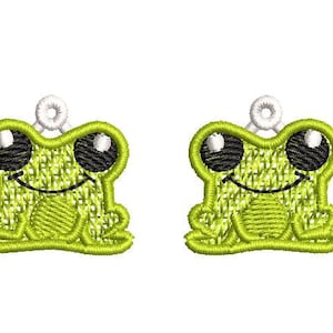 May include: Two green frog charms with black eyes and white accents. The frogs are sitting with their legs outstretched and have a smiling expression.