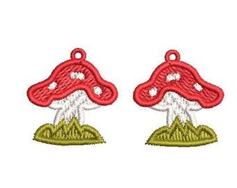 Op de afbeelding: Twee rode en witte paddestoelcharms met witte stippen en groen gras. De charms zijn perfect om een vleugje whimsy toe te voegen aan sieraden of knutselwerk.