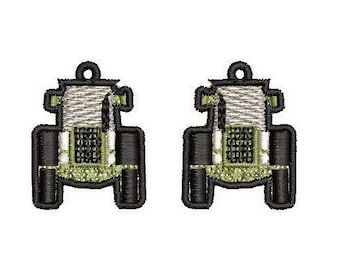 Pode incluir: Dois pingentes em forma de trator preto e verde com contorno branco. Os pingentes têm um pequeno laço na parte superior para prender a um colar ou pulseira.