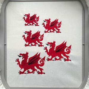 May include: Five red embroidered Welsh dragons on a white fabric background. The dragons are of varying sizes and are arranged in a staggered pattern.