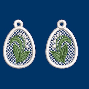 Puede incluir: Un par de pendientes ovalados blancos con un delicado diseño de encaje y un motivo floral de lirio de los valles verde.