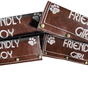 May include: Four brown leather dog leash tags with white stitching and paw prints. Two tags read "Friendly Boy" and two tags read "Friendly Girl".