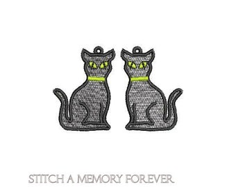 May include: Two black cat earrings with yellow eyes and a green collar. The cats are sitting with their tails curled around their legs.
