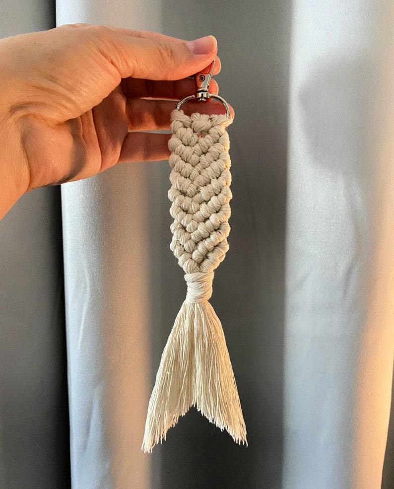 May include: A white macrame keychain with a tassel in the shape of a fish tail.