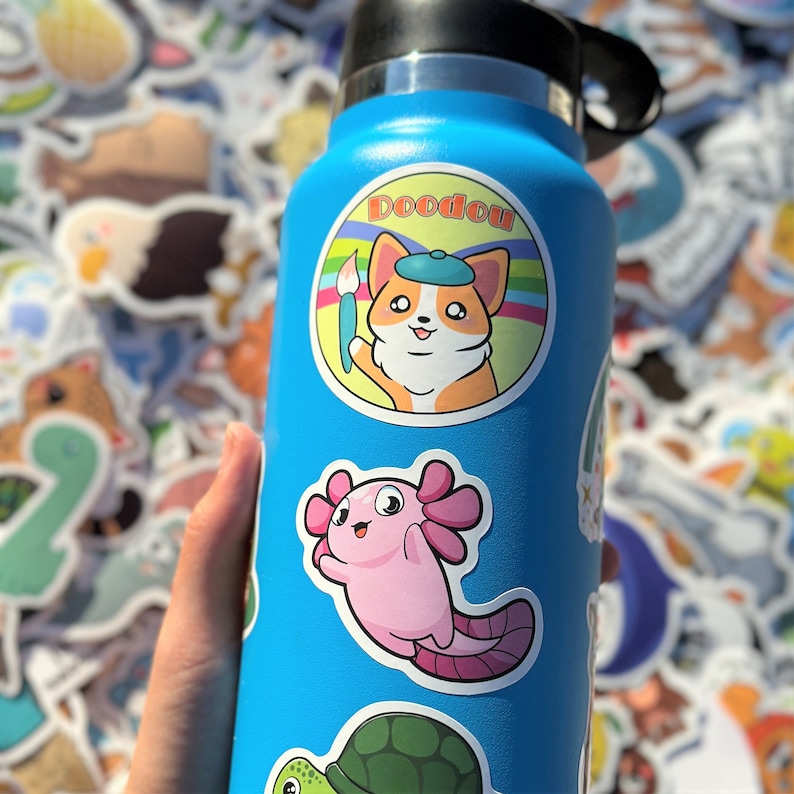 May include: A blue water bottle with a variety of colorful stickers. The stickers feature a cartoon dog, a cartoon axolotl, a turtle, and the text "Doodou".