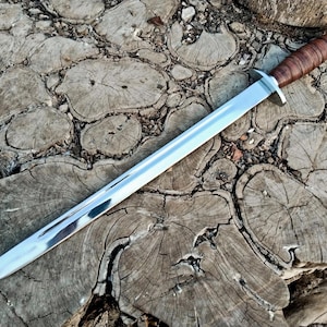 May include: A silver-colored knife with a brown leather handle. The knife is lying on a wooden surface.