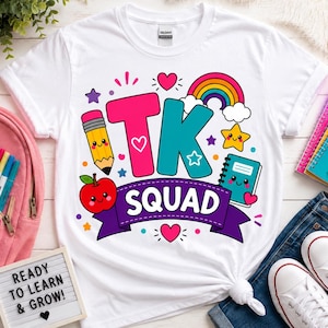 May include: A white short-sleeve t-shirt featuring a colorful graphic print that reads TK SQUAD in large pink and teal letters. The design includes a yellow pencil, a red apple, a teal notebook, a rainbow, a yellow star, and several small hearts.
