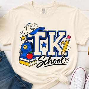 May include: A cream-colored short-sleeve t-shirt featuring a graphic with the text TK School. The design includes a blue backpack with a smiley face, a red apple, stacked books, a yellow pencil, a baseball cap, and stars in blue and yellow.