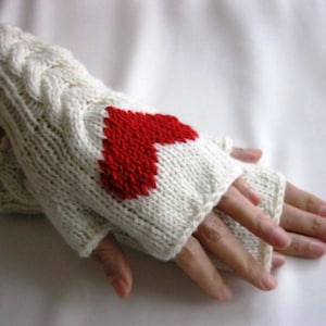 Weiße fingerlose Armstulpen aus handgestrickter Wolle mit einem roten Herz