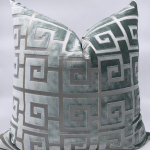 May include: A decorative throw pillow with a geometric pattern in shades of green and silver. The pillow is made of a soft, textured fabric.