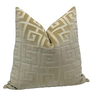 May include: A decorative throw pillow with a geometric pattern. The pillow features a repeating square design in a light beige color, creating a textured appearance. The pillow is a square shape and appears to be made of a soft fabric.