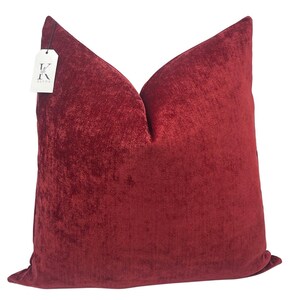 May include: A deep red velvet pillow with a subtle textured pattern. The pillow is square shaped and has a simple design.