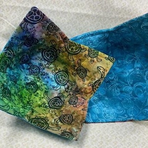 May include: Two fabric bowls with a sea turtle pattern. One bowl is blue with a white floral design, the other is a multi-colored design with a green, blue, and yellow background.