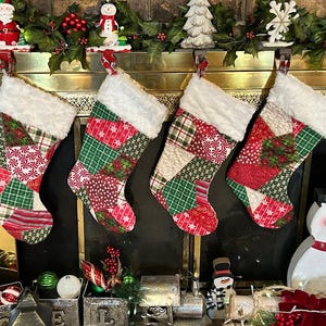 May include: Four red, green, and white patchwork Christmas stockings hang on a gold fireplace mantel. The stockings have a white faux fur cuff. A snowman figurine sits on the hearth below the stockings.
