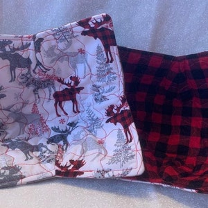 May include: Two quilted pot holders. One is white with a red and gray moose pattern. The other is red and black buffalo plaid.