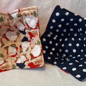 May include: Two quilted pot holders. One is red with a gnome pattern and the words "Timber" on it. The other is black with white polka dots.