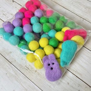 Peut inclure: Un sac en plastique transparent rempli de boules de feutre colorées dans des tons de rose, violet, vert, jaune et bleu. Il y a aussi une forme de Peep en feutre violet.