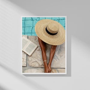 Könnte beinhalten: Ein Gemälde zeigt eine Person, die sich an einem Pool entspannt. Ein breitkrempiger Strohhut mit schwarzem Band bedeckt den Kopf. Ein offenes Buch liegt daneben, und ein goldenes Armband schmückt das Handgelenk. Das Poolwasser ist ein helles Türkis.
