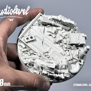 May include: A 100mm diameter round, white, resin base for miniature wargaming. The base features a detailed, ruined cityscape design with rubble, debris, and broken structures.