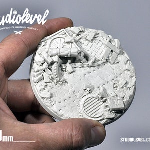 May include: A white, 88mm round, resin base for miniature wargaming. The base features a detailed, ruined cityscape design with rubble, pipes, and a manhole cover.