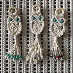 May include: Three white macrame owl keychains with wooden rings. The owls have turquoise beads for eyes. One keychain has turquoise beads on the tassel, one has red and turquoise beads, and one has only turquoise beads.