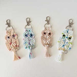 May include: Four macrame owl keychains in pastel colors. Each owl has a silver-tone clasp, bead eyes, and a small tassel. The owls are in shades of pink, blue, and beige, with a white background.