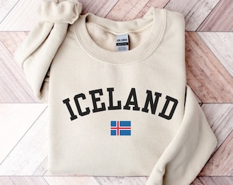 Puede incluir: Una sudadera beige con la palabra "ICELAND" impresa en letras negras con la bandera islandesa debajo.