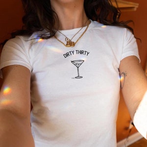 May include: White t-shirt with the text "Dirty Thirty" and a martini glass graphic.