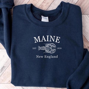 May include: A navy blue sweatshirt with a white graphic design featuring a lobster and the text "Maine Est 1820 New England".