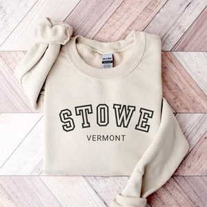 May include: A beige sweatshirt with black text that reads "STOWE VERMONT".