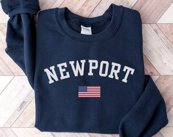May include: Navy blue sweatshirt with the word "NEWPORT" in white letters and a small American flag printed on the front.