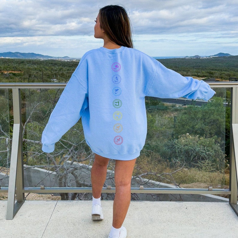 May include: A light blue sweatshirt with a rainbow design of seven chakras on the back. The chakras are represented by symbols and colors.