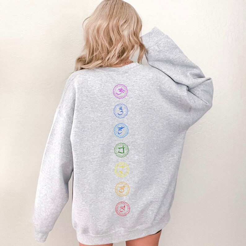 May include: A gray sweatshirt with a vertical row of seven colorful chakra symbols printed on the back. The symbols are in a rainbow pattern, starting with red at the bottom and ending with purple at the top.