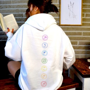 May include: White hooded sweatshirt with a rainbow colored chakra symbols printed on the back. The symbols are in a vertical line and include Om, Svadhisthana, Manipura, Anahata, Vishuddha, Ajna, and Muladhara.