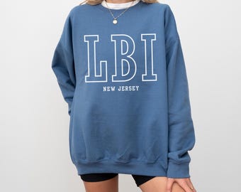 May include: A blue sweatshirt with the white text "LBI" above "NEW JERSEY". The sweatshirt is a solid blue color and has a crew neck. The sleeves are long and the fit is loose.