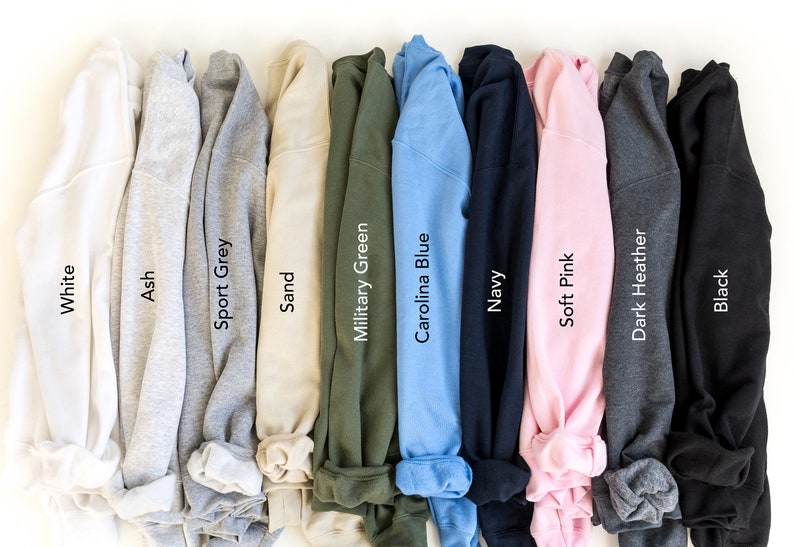 May include: A selection of ten folded sweatshirts in various colors, including white, ash, sport grey, sand, military green, carolina blue, navy, soft pink, dark heather, and black.