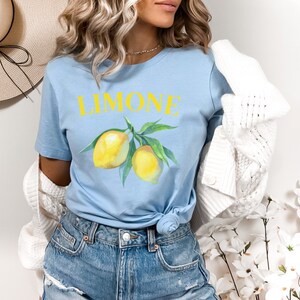 May include: Light blue t-shirt with the word "LIMONE" in yellow and a watercolor illustration of lemons on a branch. The shirt is a casual style, suitable for everyday wear.