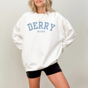 May include: White sweatshirt with a blue graphic print that says "Derry Maine" in a collegiate font.