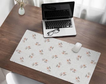 Puede incluir: Una alfombrilla de escritorio blanca con un sutil patrón floral en tonos marrones y grises. La alfombrilla está sobre un escritorio de madera con un portátil y unas gafas encima.