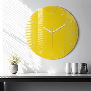Può includere: Un orologio da parete circolare con un quadrante giallo brillante e indicatori delle ore bianchi. L'orologio presenta sottili lancette bianche per ore, minuti e secondi centrate sul quadrante. Il design è semplice e privo di numeri.