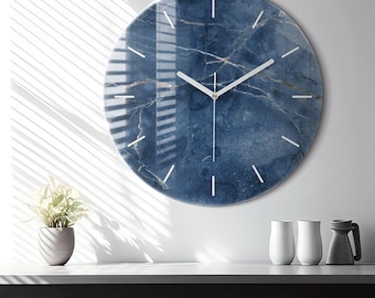 May include: A circular wall clock featuring a deep blue marble pattern with white veining. The clock face has a smooth, glossy finish with thin, white, minimalist hour markers and simple white hour, minute, and second hands centred.