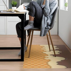 May include: A waffle-patterned floor mat with a brown and white chocolate-like design. The mat is under a chair with a person sitting on it.