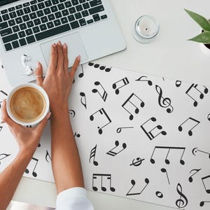 May include: A white desk mat with a black musical note pattern. A laptop, a cup of coffee, and a small plant are on the desk.