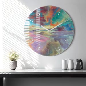 Könnte beinhalten: Eine runde Wanduhr mit einem lebendigen, abstrakten Himmelsdruck in gemischten Farbtönen von Orange, Türkis, Violett und Blau. Das Zifferblatt hat dünne weiße Stundenmarkierungen und zwei einfache weiße Zeiger vor dem farbenfrohen Hintergrund.
