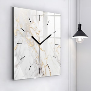 May include: A square wall clock featuring a white marble pattern with gold veining. The clock face has thin black hour markers and black hands. The surface has a glossy finish, reflecting light across the marble design and the black clock hands.