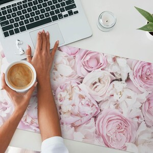 Peut inclure: Un tapis de bureau floral rose et blanc avec une tasse de café dessus. Le tapis est fait d'un matériau doux et texturé et présente une variété de roses roses et blanches.