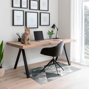Op de afbeelding: Een licht houten bureau met zwarte metalen poten en een zwarte bureaustoel. Een kat zit op het bureau naast een laptop. Er hangen ingelijste foto's aan de muur achter het bureau.