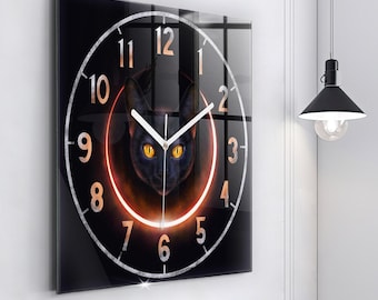 May include: A square wall clock with a glossy black surface featuring a central illustration of a black cat with glowing yellow eyes. A bright orange circular ring surrounds the cat, and white numbers from 1 to 12 are arranged in a circle.