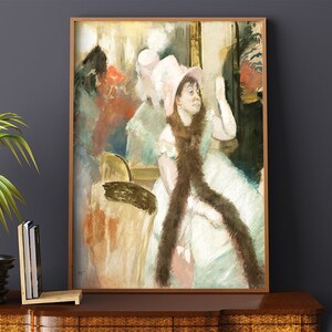 Puede incluir: Una impresión enmarcada de una pintura impresionista. La obra representa a una mujer con un vestido blanco y un sombrero rosa, con una bufanda marrón. El fondo presenta figuras y colores borrosos, con un marco de madera.